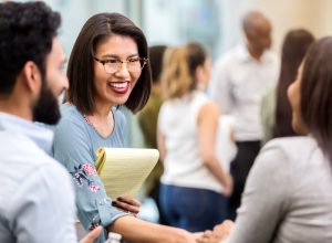 cheerful young businesswoman stands with an unrecognizable coworker in a crowded office building and smiles as she shakes hands with her new unrecognizable client