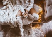 woman sitting on bed next to twinkly lights and hot chocolate