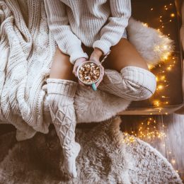 woman sitting on bed next to twinkly lights and hot chocolate