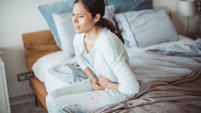 Woman holding her stomach in pain sitting on edge of bed