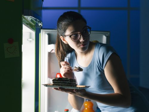 Woman sneaking into the fridge for a late night snack of cake hoping not to get caught