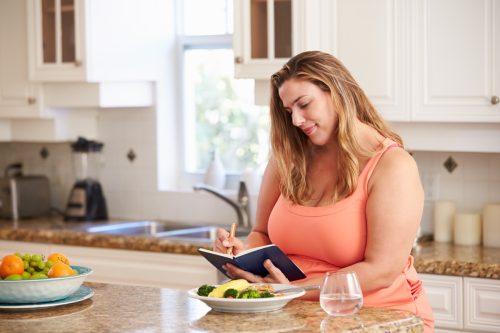 Woman writing in food log journal before eating her meal
