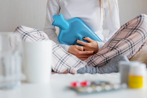 Woman clutching a hot water bottle against her stomach to alleviate cramps from period pain