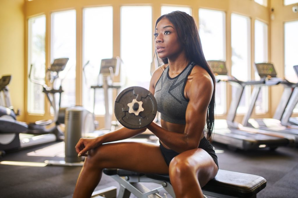 Woman sitting at the gym lifting a weight concentrating