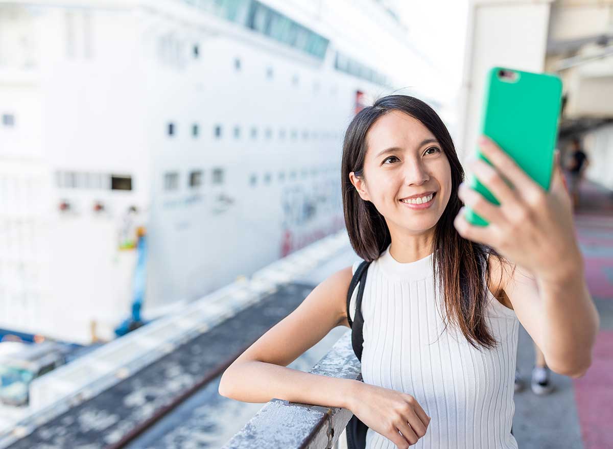 a young asian woman smiles for a selfie with a cruise ship