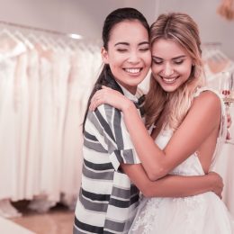two women hugging in wedding gown and casual clothing at bridal shop