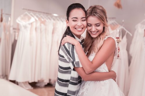two women hugging in wedding gown and casual clothing at bridal shop
