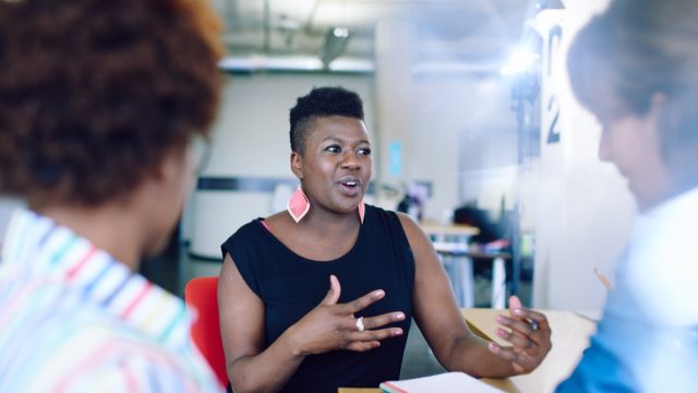 30-something female colleagues talking at work, black woman talking at work