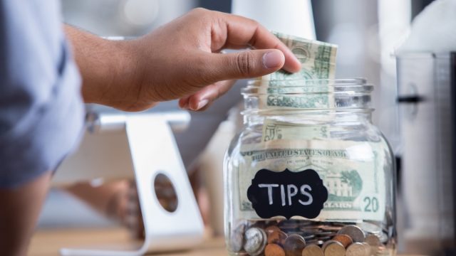 Unrecognizable male coffee shop customer places cash into a tip jar.