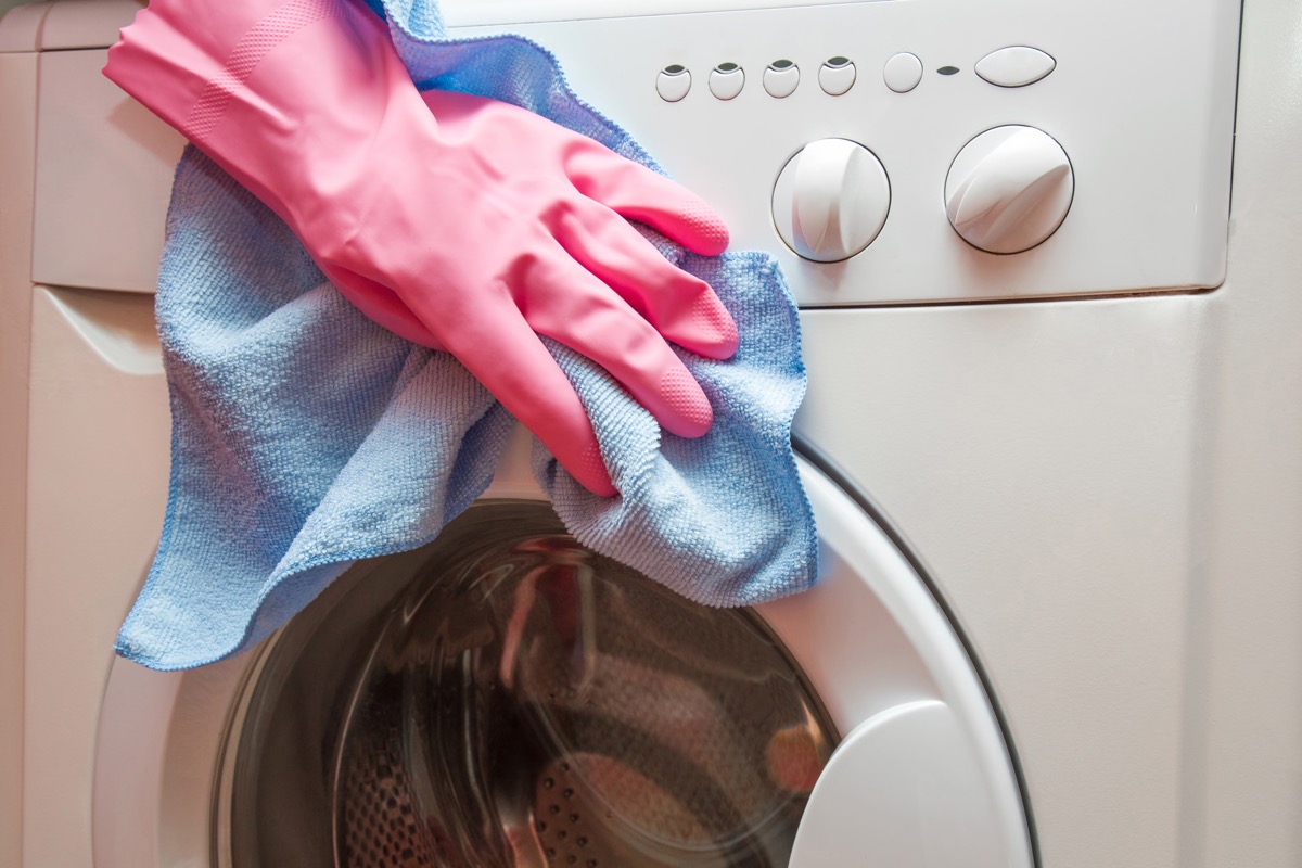 woman's hand with gloves cleaning exterior of washing machine