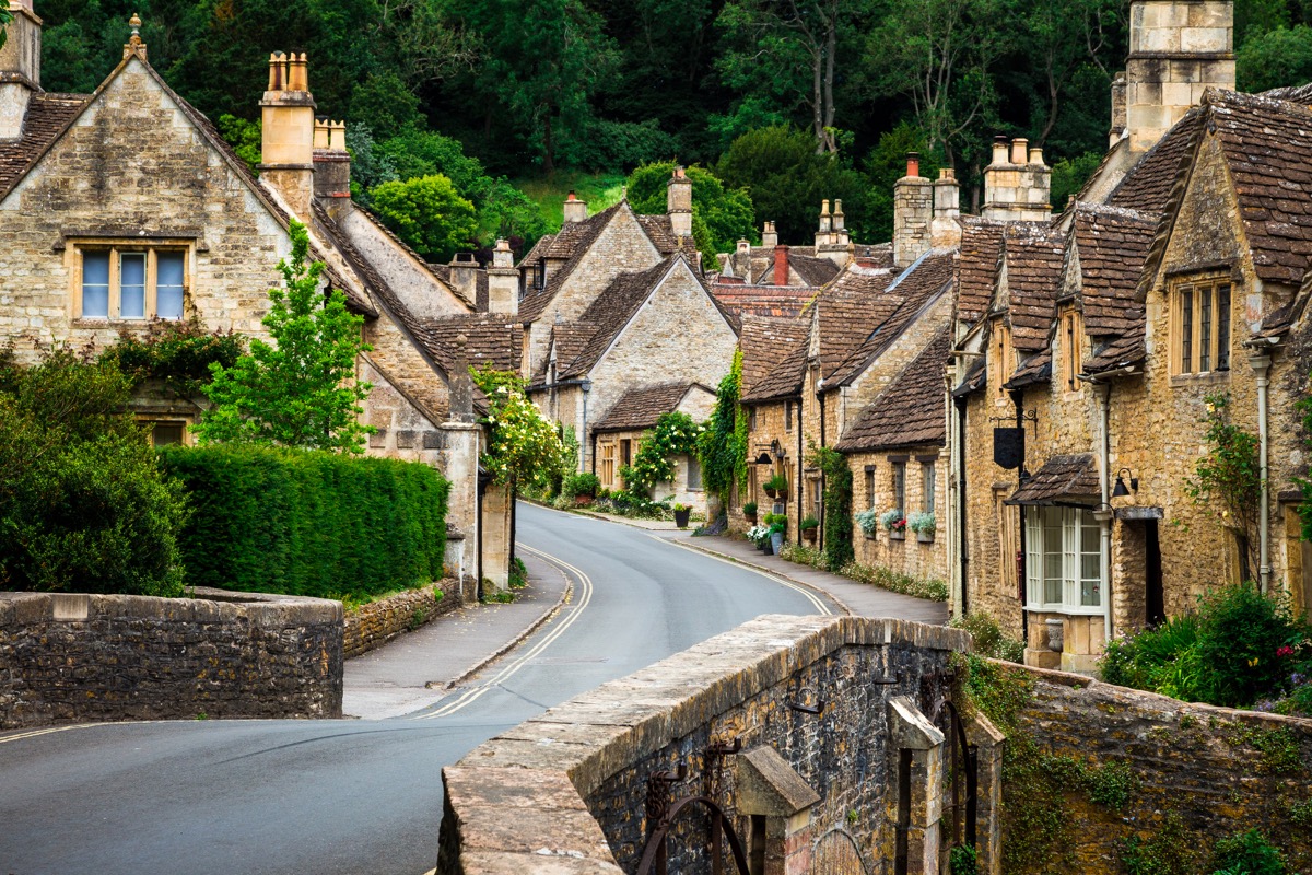 color image depicting a traditional English village in the Cotswolds area of southwest England. The cosy little brick cottages line the narrow road, and there is also a quaint bridge spanning a little stream. Room for copy space.