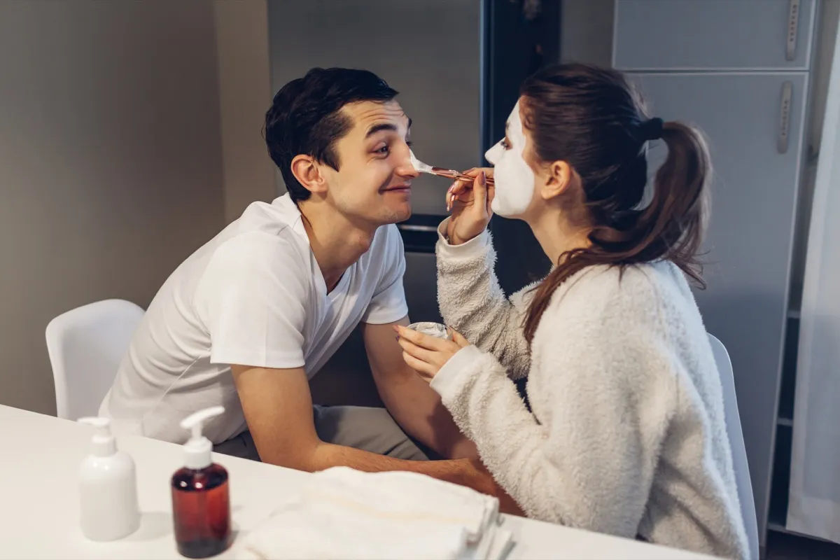 woman applying a clay face mask to her boyfriend's face