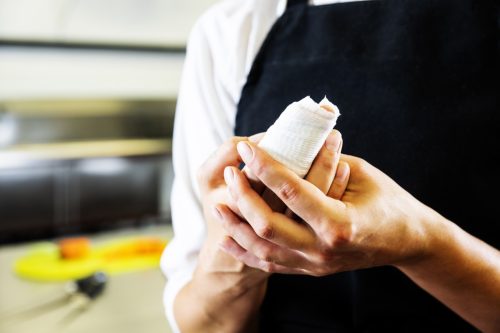 a real professional chef in pain after cutting her finger slicing carrots. She is in a real commercial restaurant or food processing kitchen. A kitchen safety concept on cuts and abrasions in the food service industry.