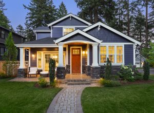 facade of dark blue home with manicured lawn, landscaping, and backdrop of trees