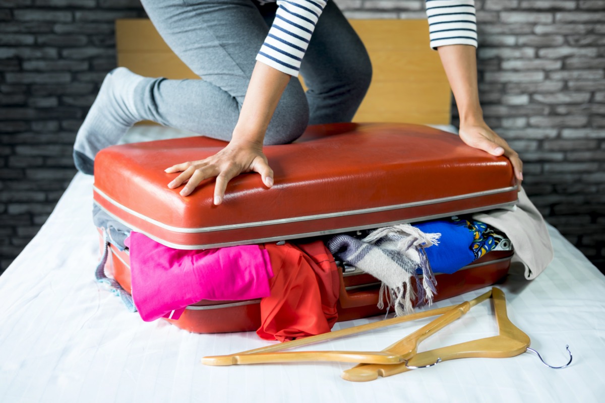 a person tries to close a full suitcase overflowing with clothes