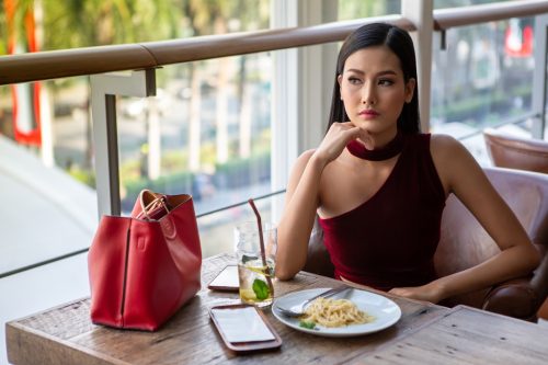 young woman sitting at a lunch place eating alone with the food in front of her, looking sad