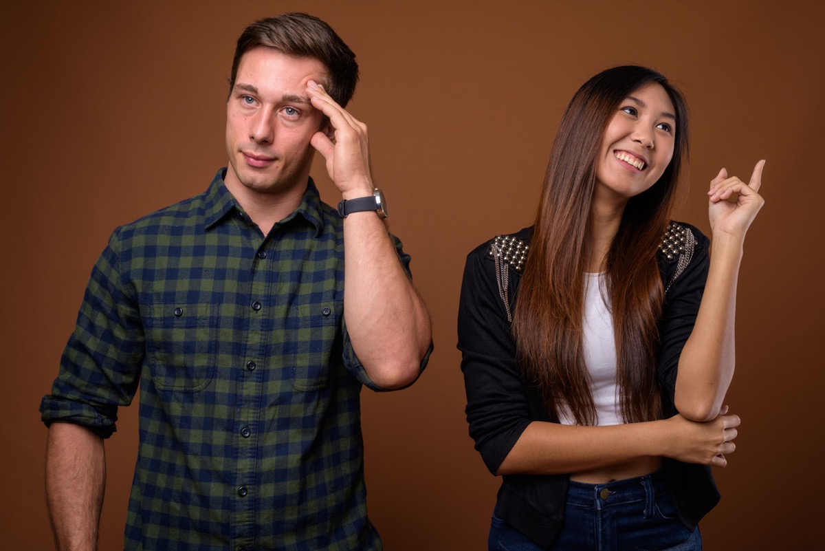 annoyed white man next to smiling asian woman on a brown background