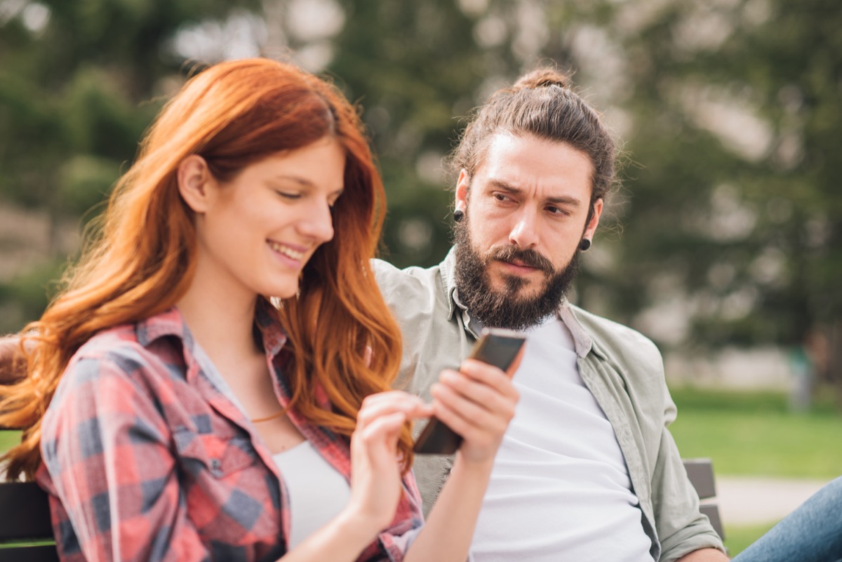 jealous man looking at his girlfriend while she's smiling at her phone