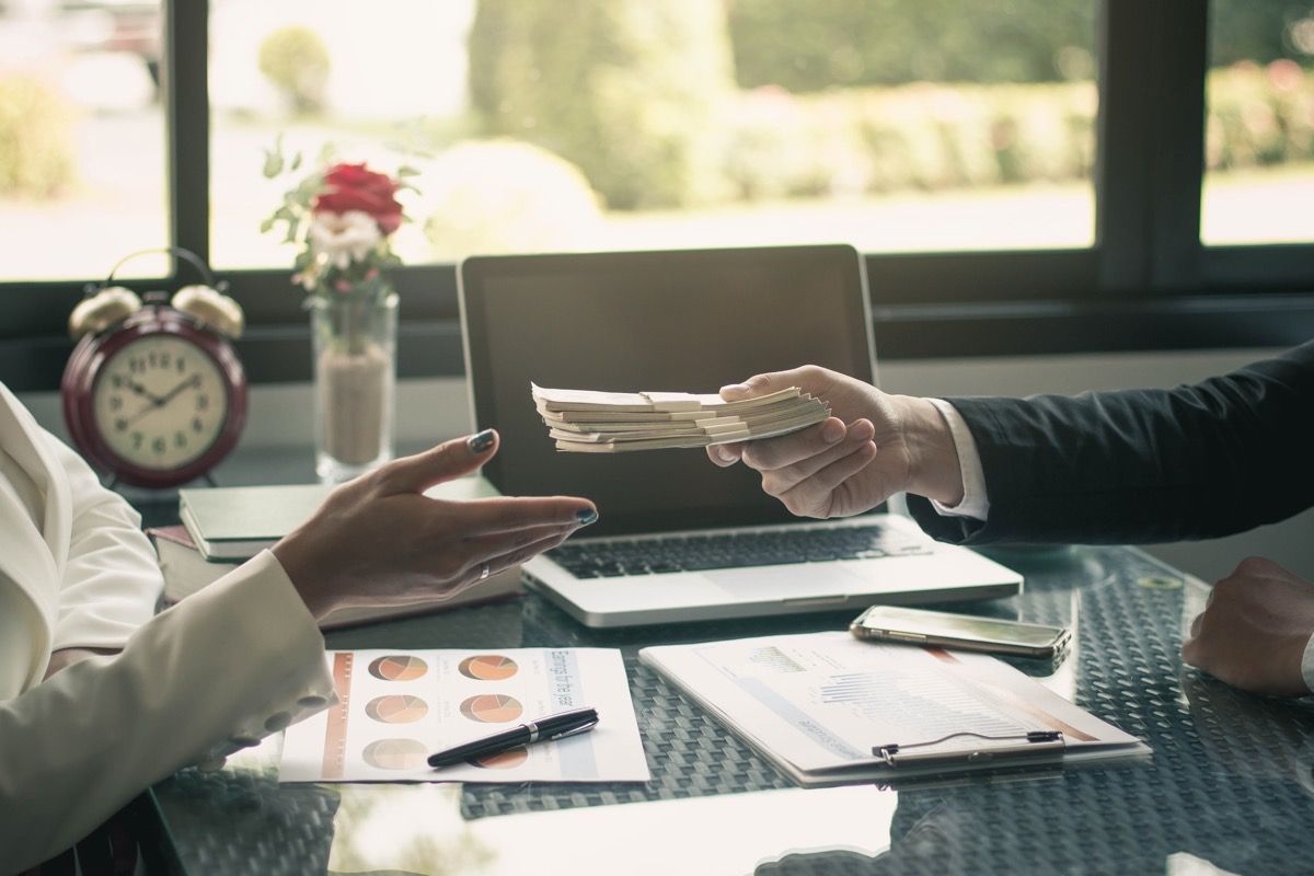 white man's hand giving stack of cash to woman