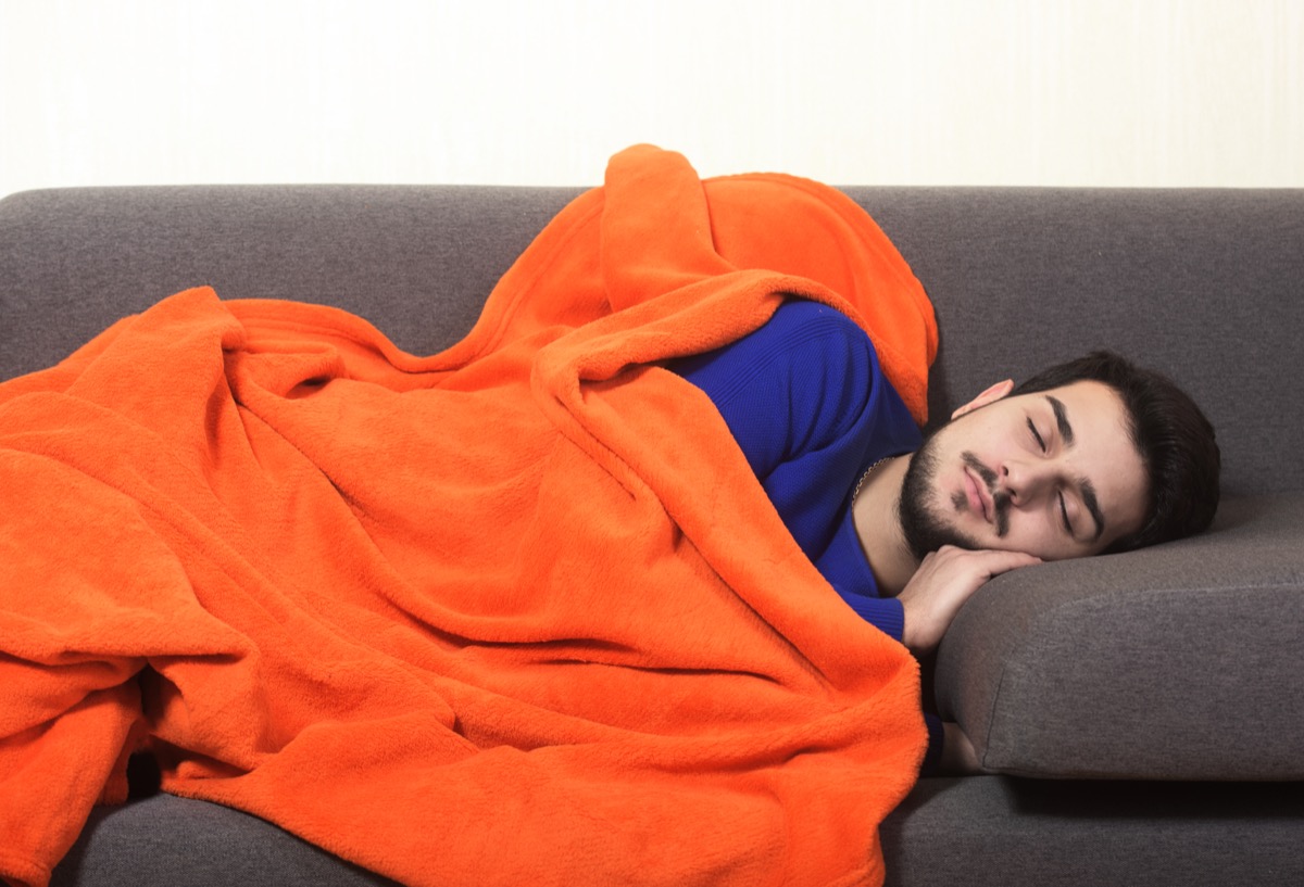 Man napping with an orange blanket on the couch