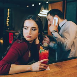 sad girl looking off while her date is on the phone at the bar