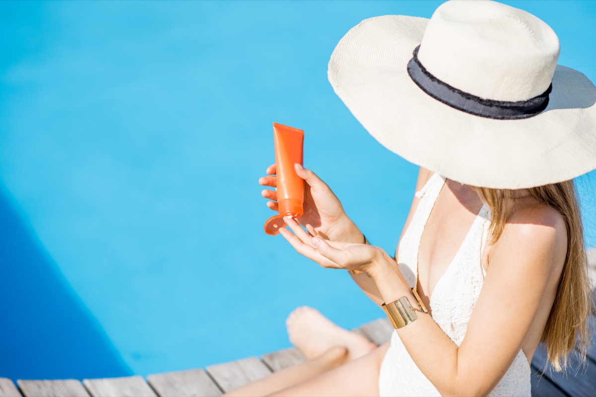 Woman applying sunscreen by the pool wearing a sun hat