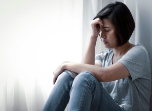 upset middle-aged asian woman sitting on floor