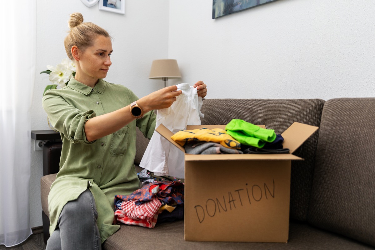 mother sitting on couch and sorting child clothes for donation