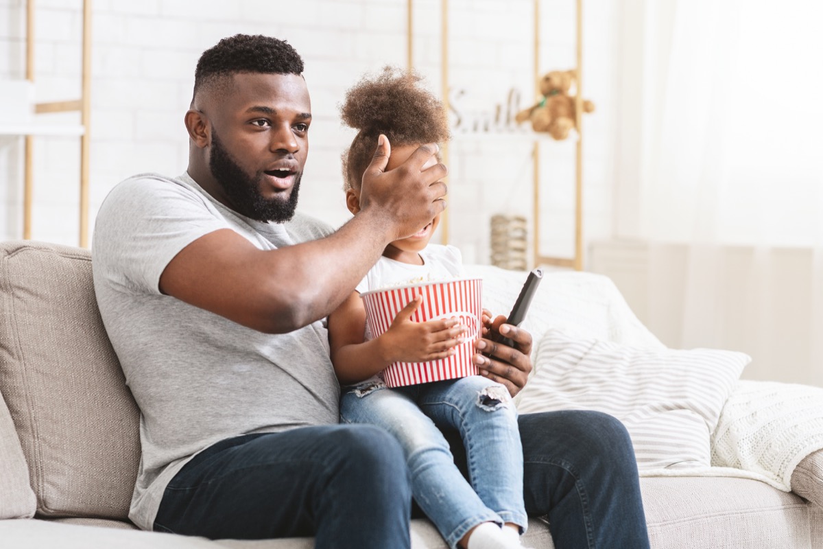 young father covering daughter's eyes while watching movie