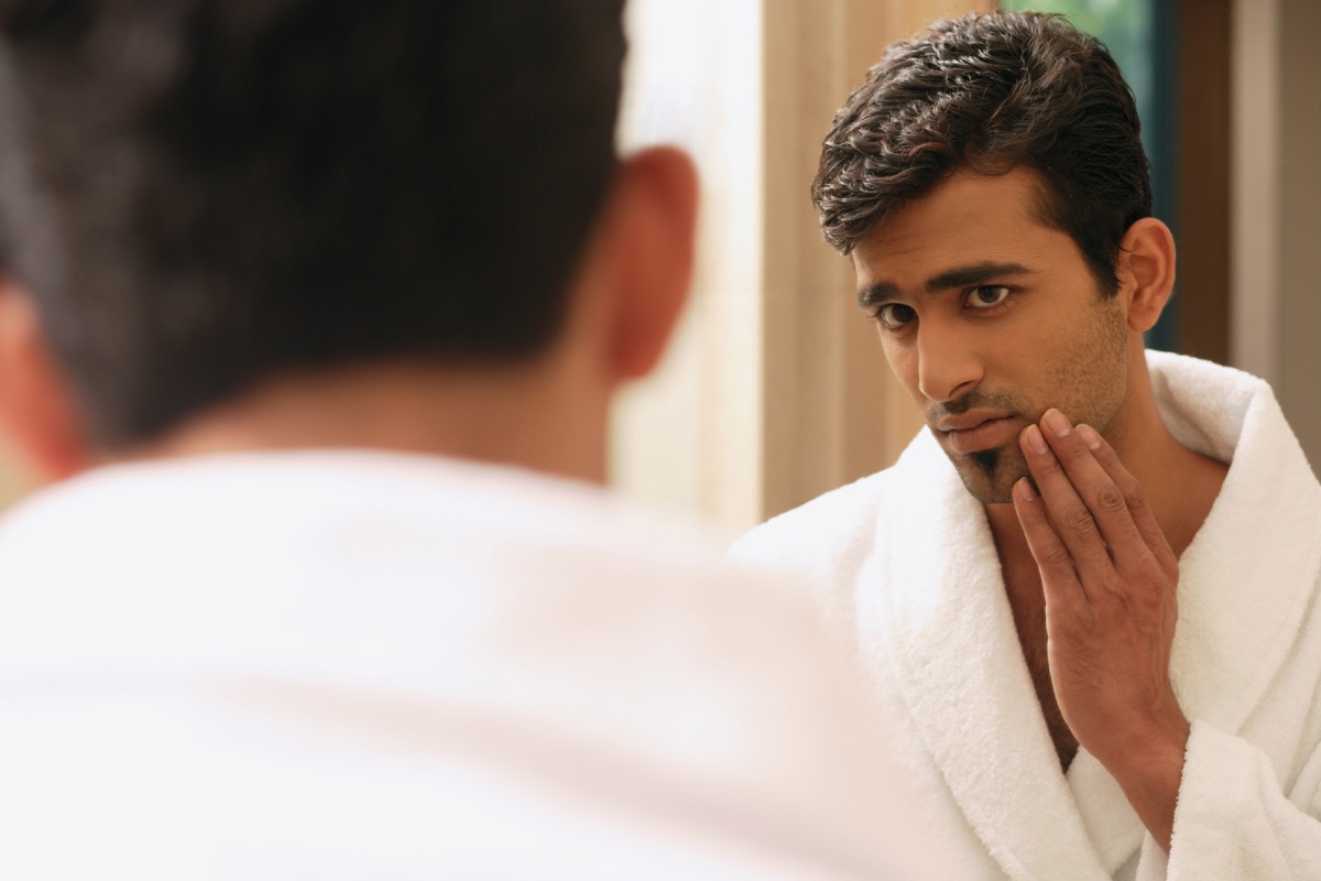 young indian man inspecting face in mirror