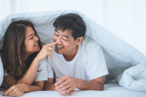 senior asian woman smiling with senior asian man underneath white comforter
