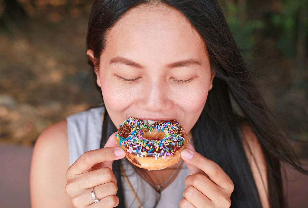 young asian woman eating sprinkled donut