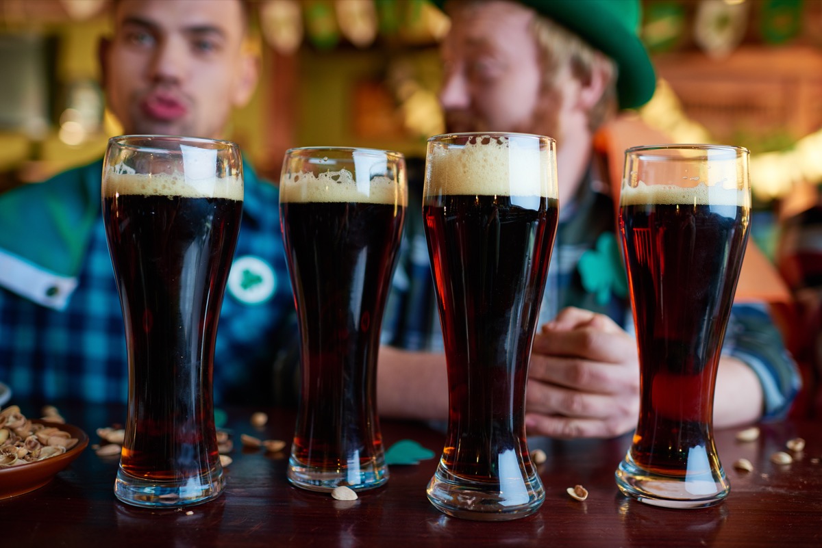 close-up of full glasses of dark beer with foam placed on table with nut shells