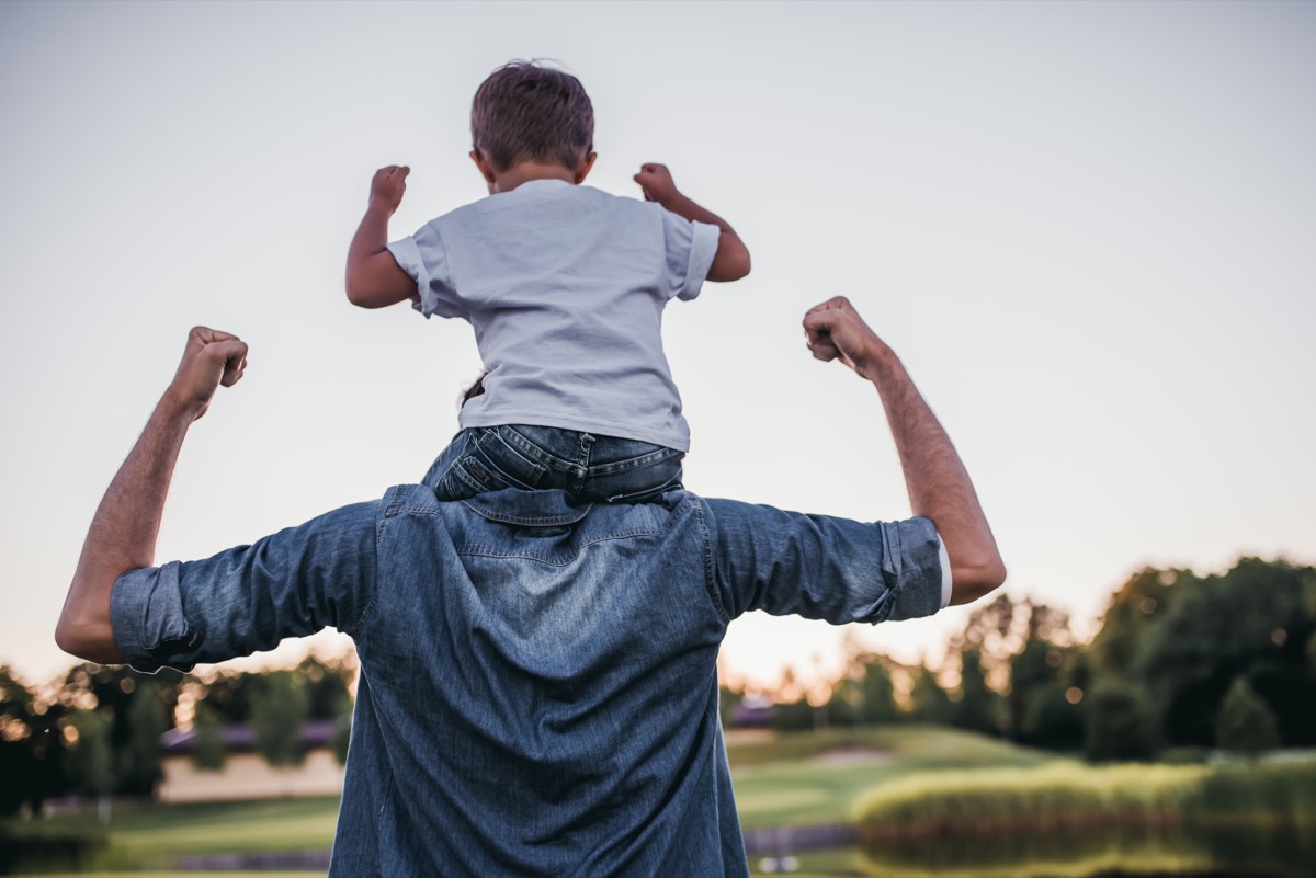 Child on father's shoulders doing muscle arms