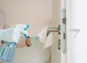 Woman in protective gloves cleaning a door handle with a disinfection spray and disposable wipes