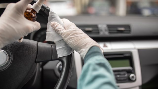 Person disinfecting and cleaning car interior with antiseptic liquid and wet disinfection wipes. Steering wheel is one of dirtiest parts in car and can contains viruses and bacteria.