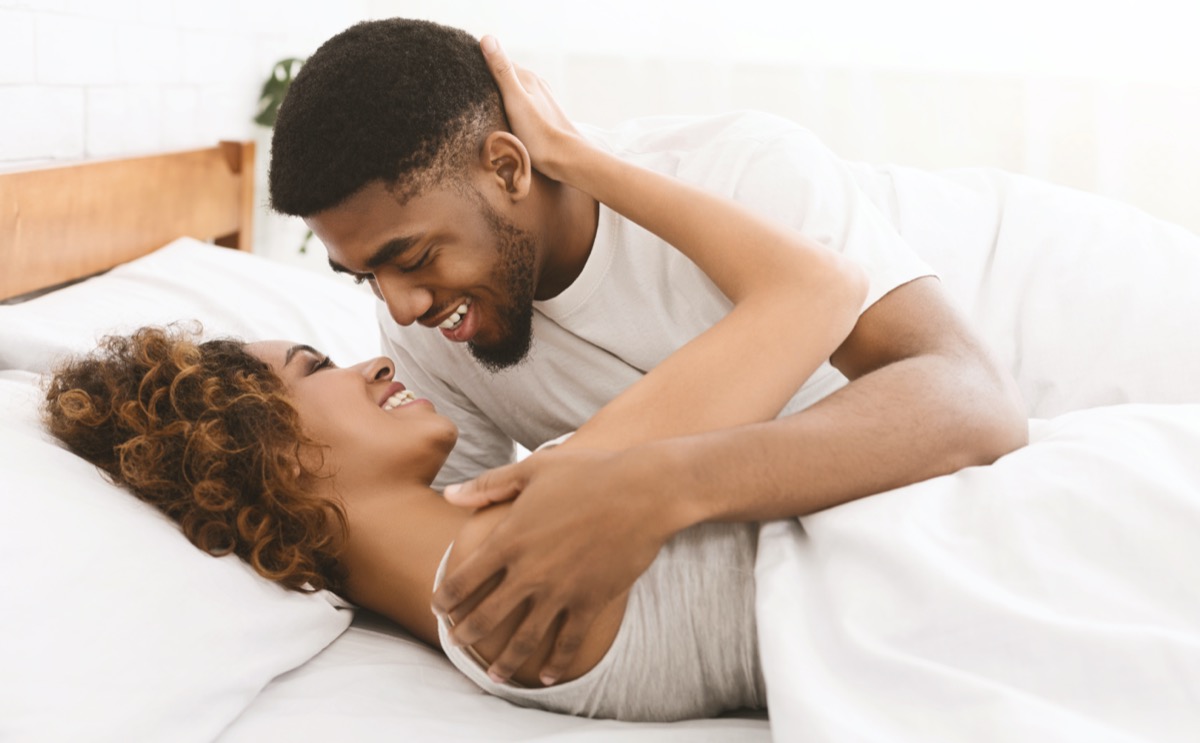 young black woman in white tank top and black man in white t-shirt looking into each other's eyes in bed