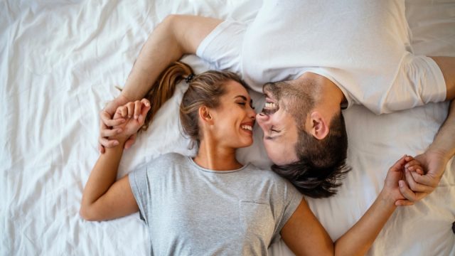 young white woman and man touching noses and laughing in bed