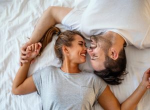 young white woman and man touching noses and laughing in bed