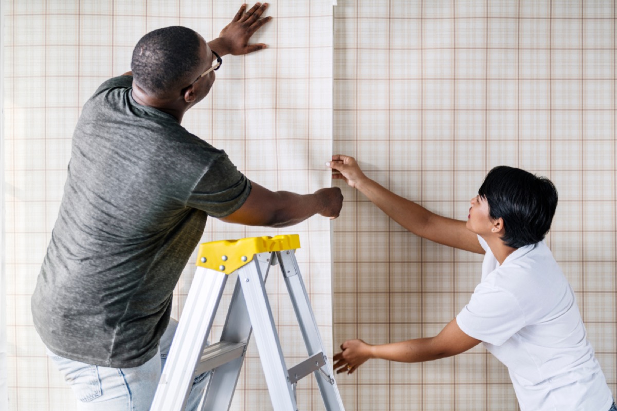 couple wallpapering together, man stands on later