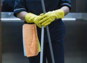 closeup of midsection of custodian's body, their hands are in gloves and they're holding a mop