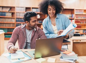 friend explaining book to classmate in library
