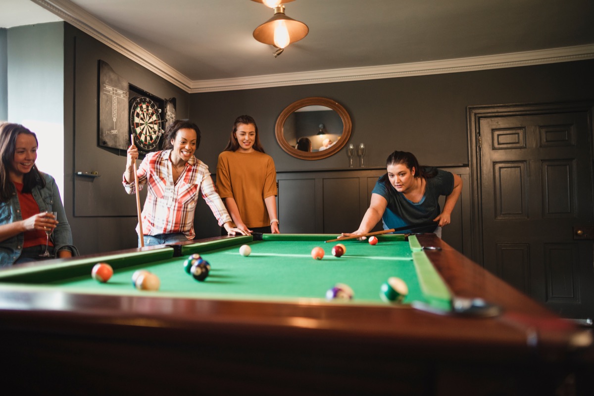 Girl friends playing pool in game room with darts