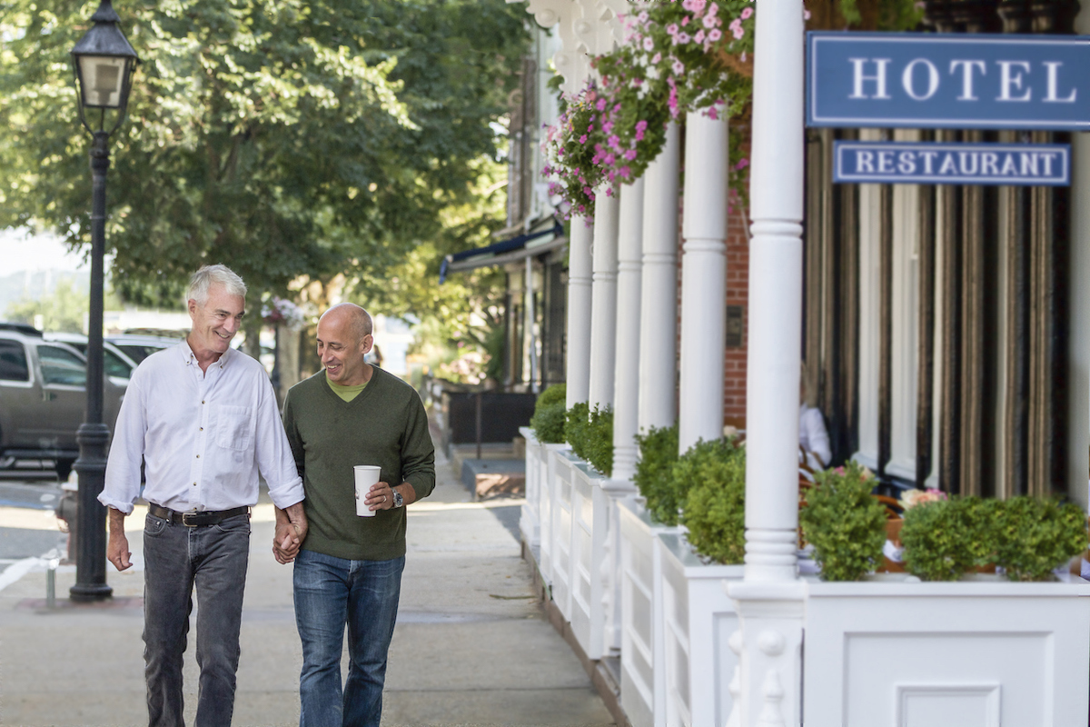 Mature, older senior gay male couple, affectionate and holding hands, walking down the main street of a small village in the Hamptons.