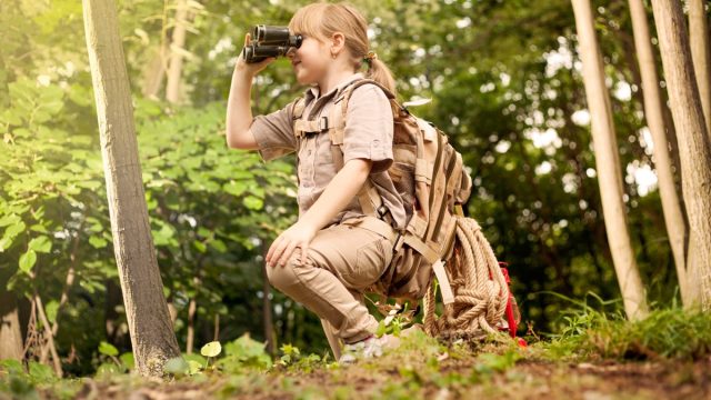 young girl scout kneeling in woods looking through binoculars