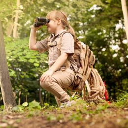 young girl scout kneeling in woods looking through binoculars