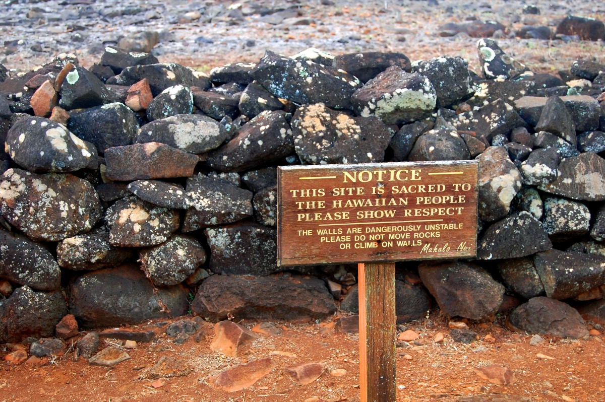 Sign posted declares this site sacred to the Hawaiian people. Wooden sign stands in front of remains of part of the Poili'ahu Heiau on the Island of Kauai, Hawaii.