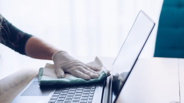 close up of gloved hand wiping down laptop to disinfect it