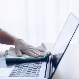 close up of gloved hand wiping down laptop to disinfect it