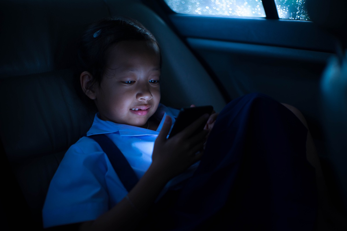 young asian girl playing on smartphone in dark car at night